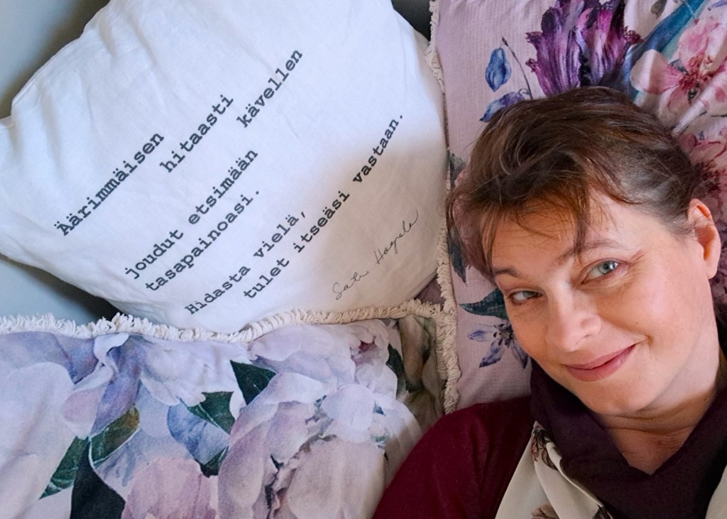 Hymyilevä henkilö lepää pää kukallisella koristetyynyllä, vieressä tyyny, jossa on runo.