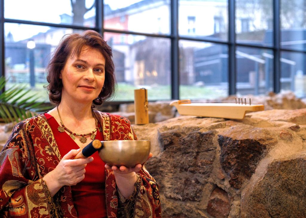 Satu Haapala Aboa Vetuksen aulassa, kädessään äänimalja, taustalla koshi ja kantele